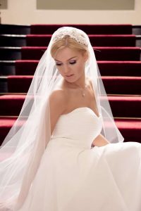 Close up of pretty bride sat on grand staircase wearing Juliet cap veil