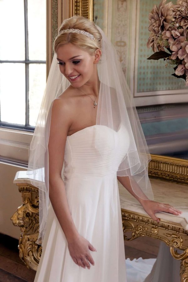 Smiling bride in grand ballroom wearing wedding veil with a scalloped edge.