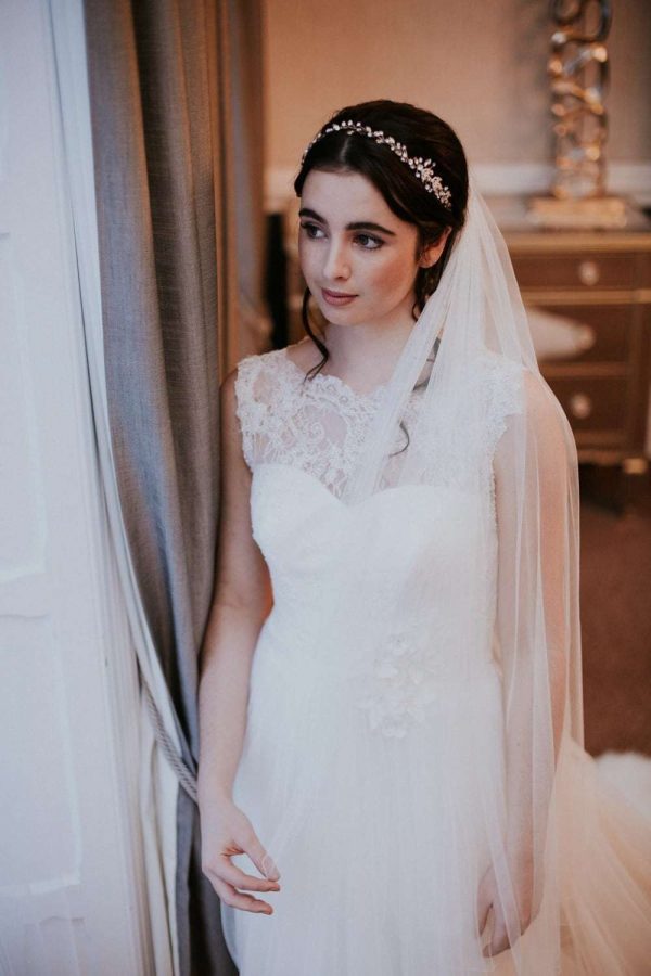 Bride looking out a window wearing wedding dress and veil in Silk Effect tulle