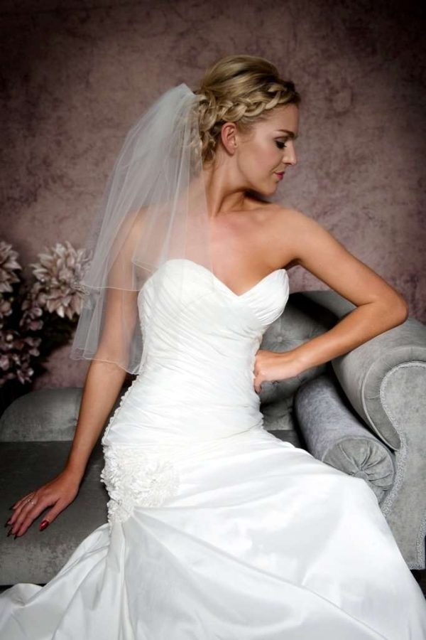 Close up of bride sitting on chaise wearing an elbow length pencil edge veil