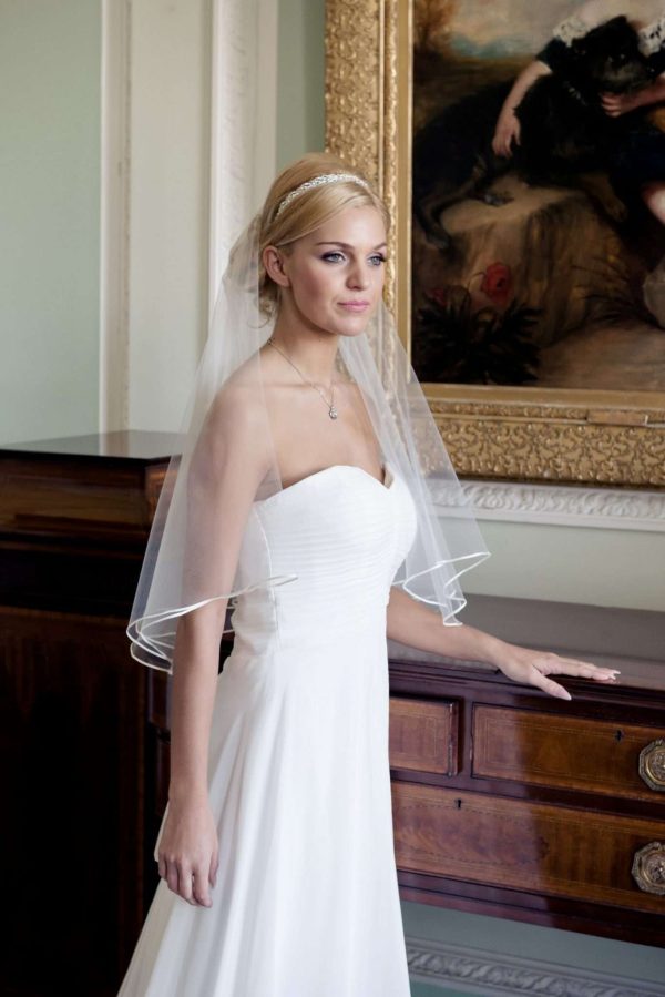 Bride wearing two layer elbow length single layer veil with ribbon edging